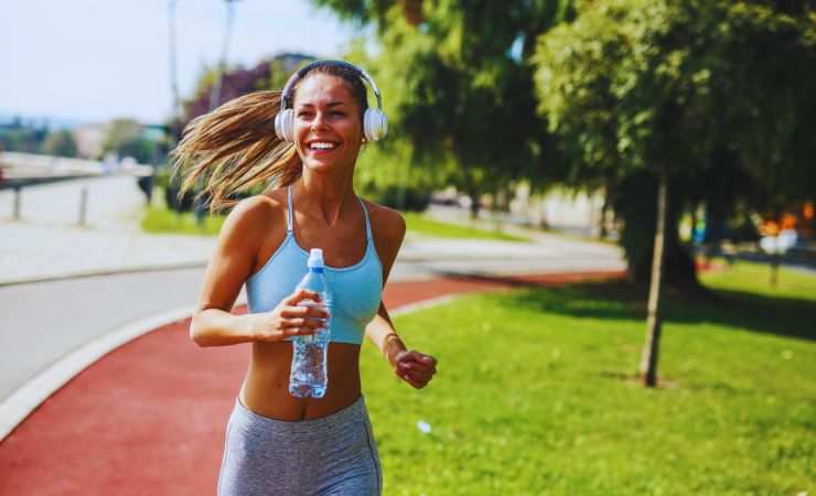 ragazza ascolta musica mentre corre con una bottiglia d'acqua in mano